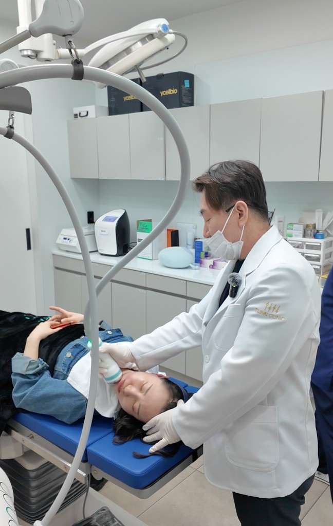 A doctor performing a facial treatment on a reclined patient